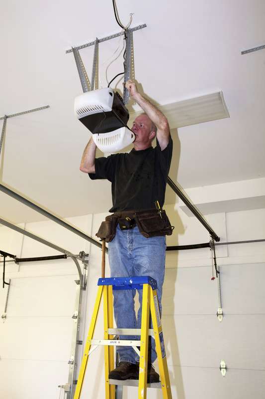Man standing on a ladder replacing garage door opener